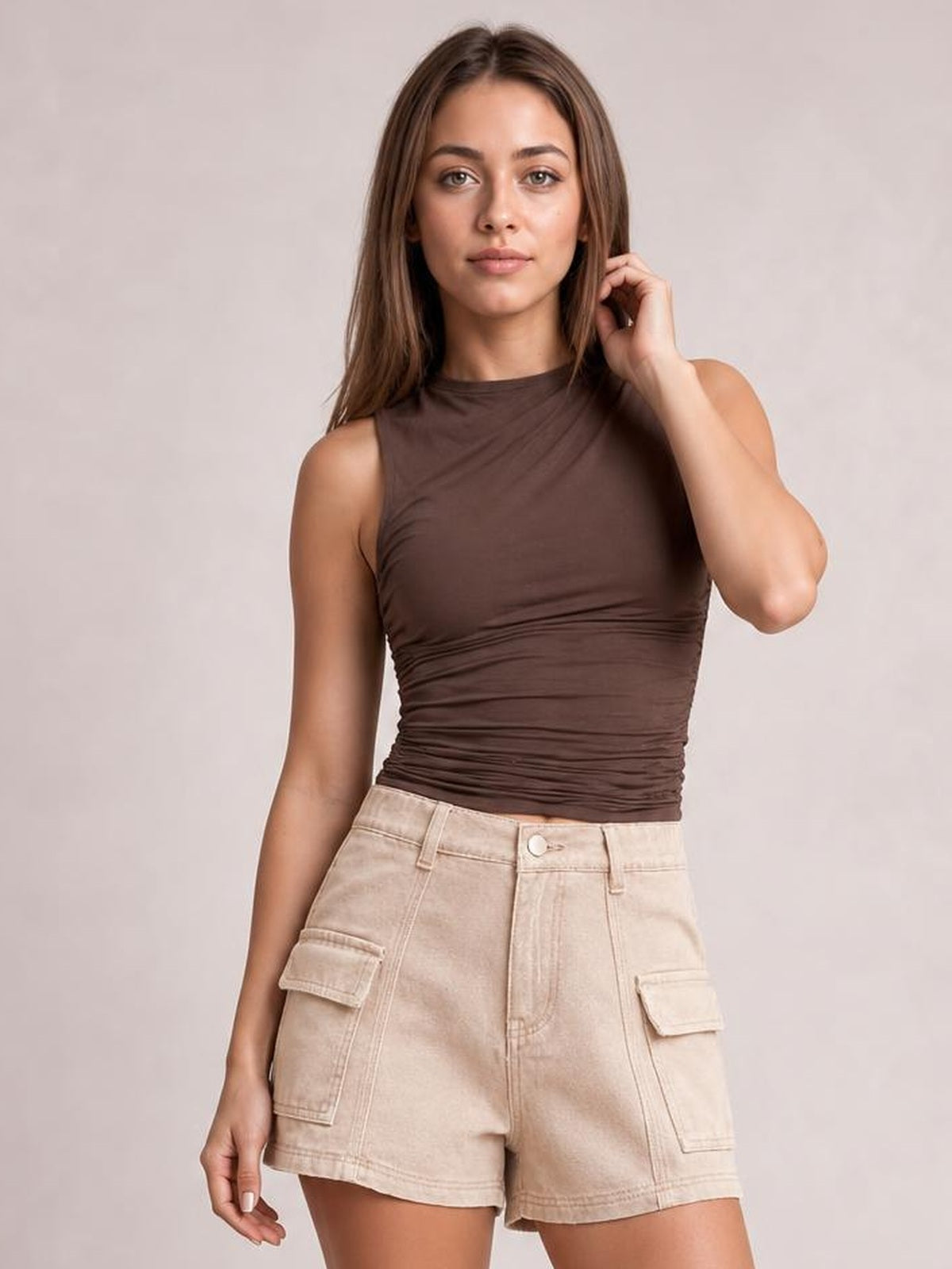 A woman modeling a sleeveless brown ribbed top and beige cargo shorts against a plain light gray studio background.