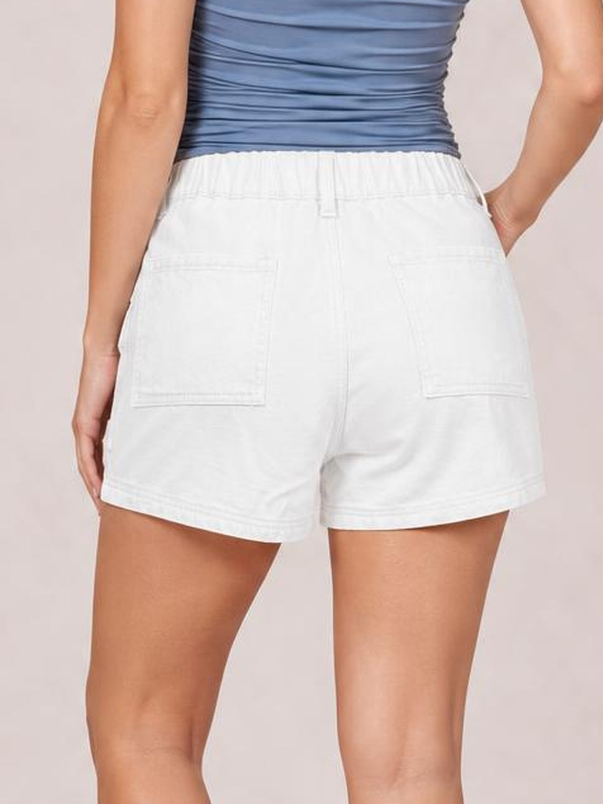 Model shown from behind wearing white high waist denim shorts with belt loops, seam details, back pockets, and a relaxed straight-leg silhouette.