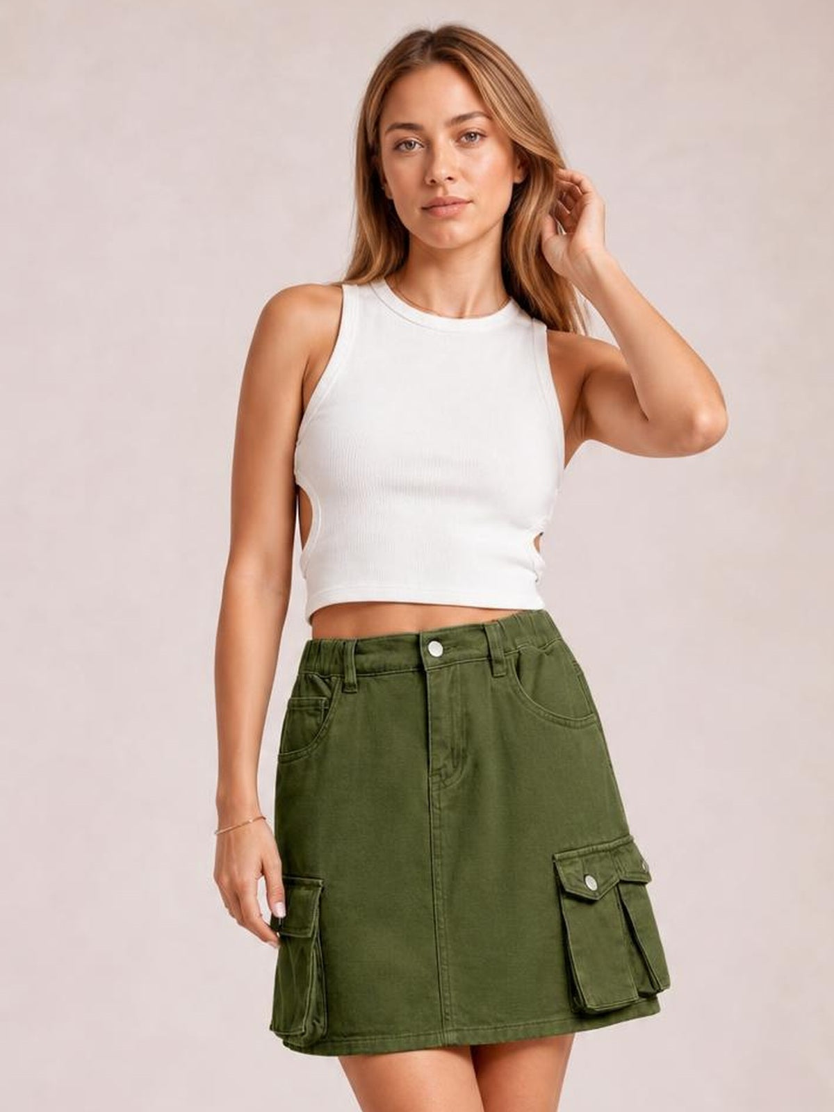 A model poses in an olive green high-waist denim skirt with belt loops, front pockets, flap cargo pockets, and a straight mini silhouette.