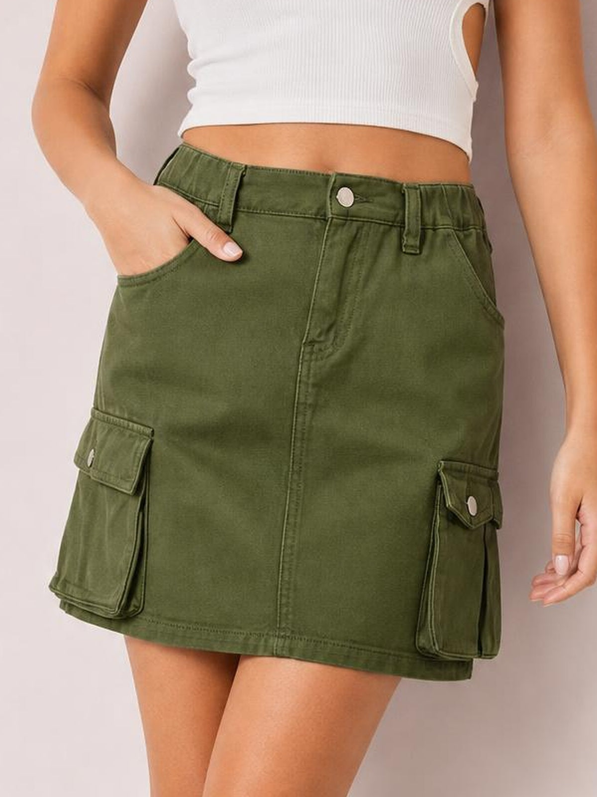 A model wears a green high-waist denim skirt with belt loops, button closure, front pockets, cargo patch pockets, and a straight mini silhouette.