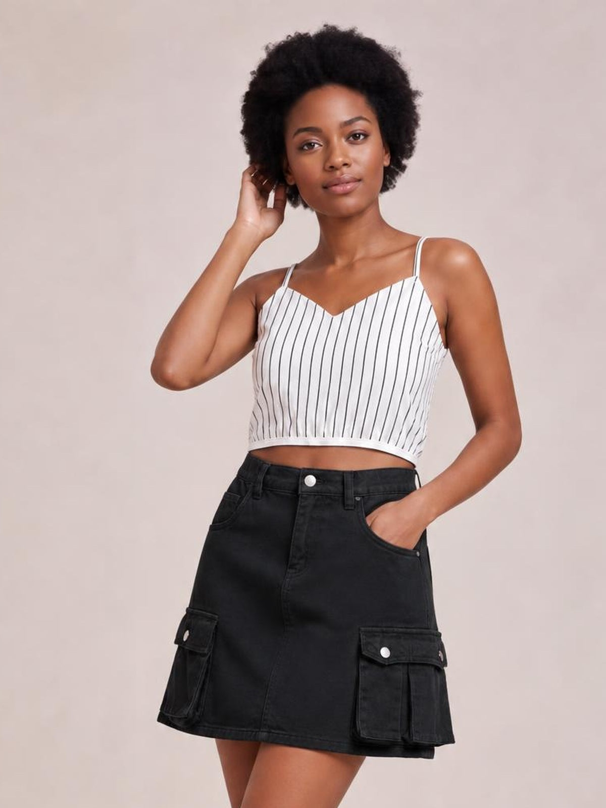 A model poses in a black high waist denim skirt with a short A-line silhouette, belt loops, front pockets, and flap cargo pockets, one hand tucked inside.