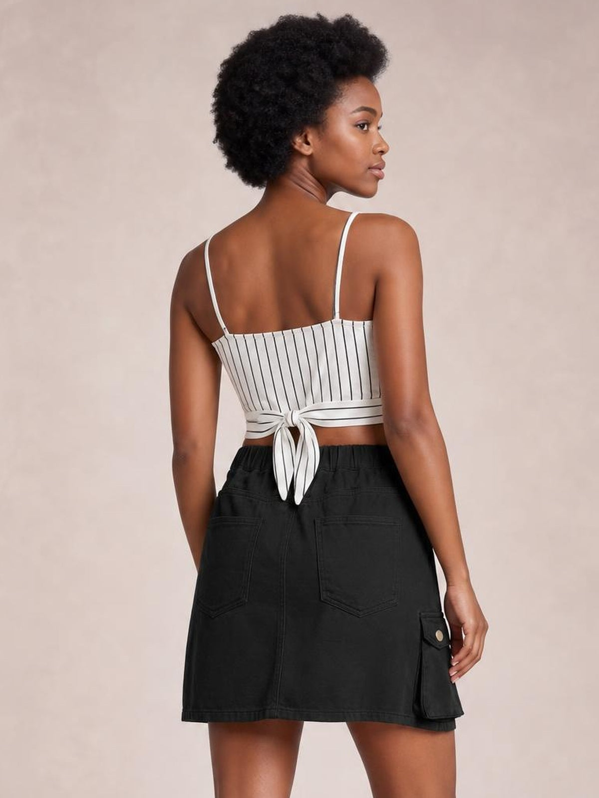 Model shown from behind in a high-waist black denim skirt with a straight silhouette, back patch pockets, and a side cargo pocket, looking over her shoulder.