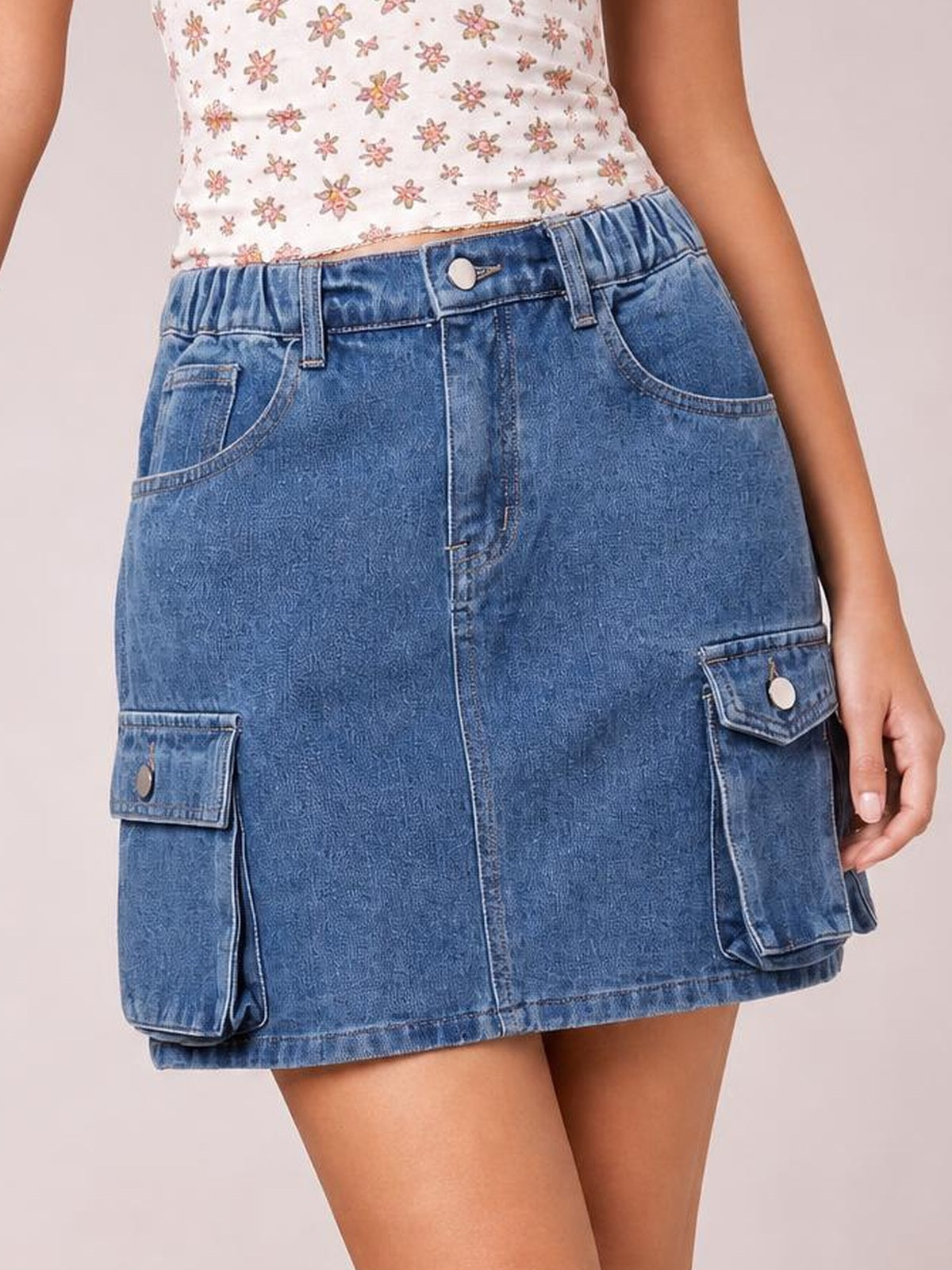 Model wears a blue high waist denim skirt with a straight mini silhouette, belt loops, button closure, front seam, and multiple flap cargo pockets.
