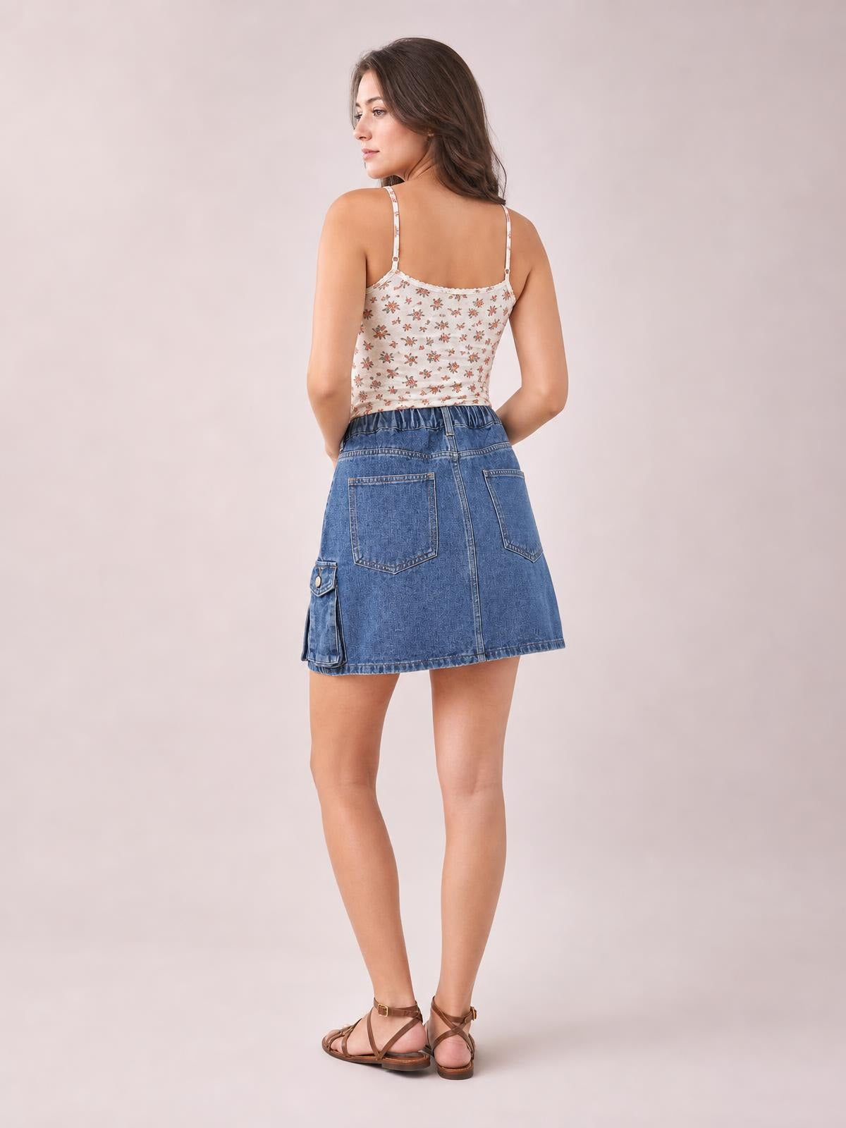 A model poses in a back view wearing a blue high waist denim skirt with a gently flared silhouette, back patch pockets, and a side cargo pocket.