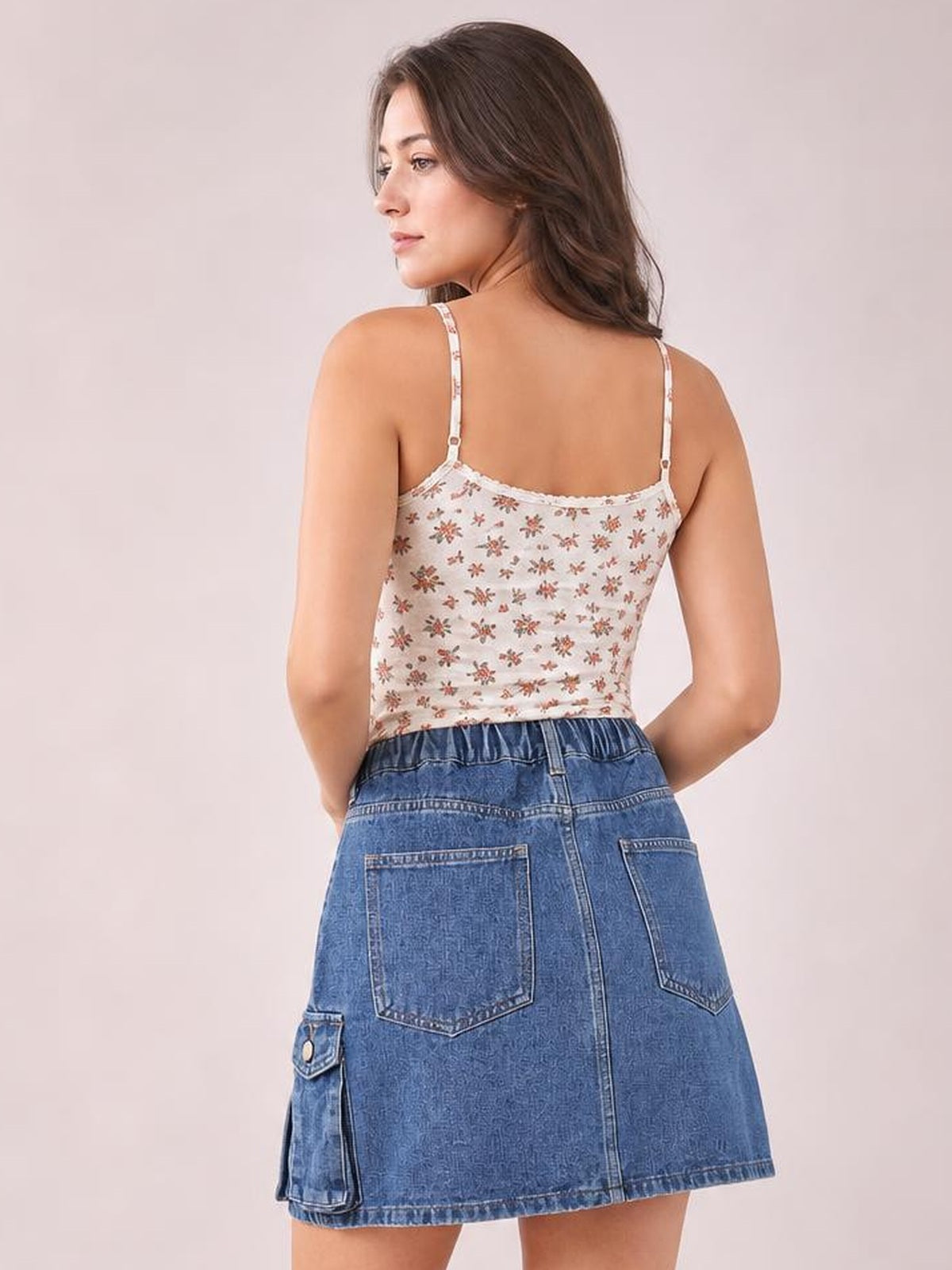 A model poses from behind in a blue high waist denim skirt with a straight silhouette, belt loops, back patch pockets, and a flap cargo pocket.