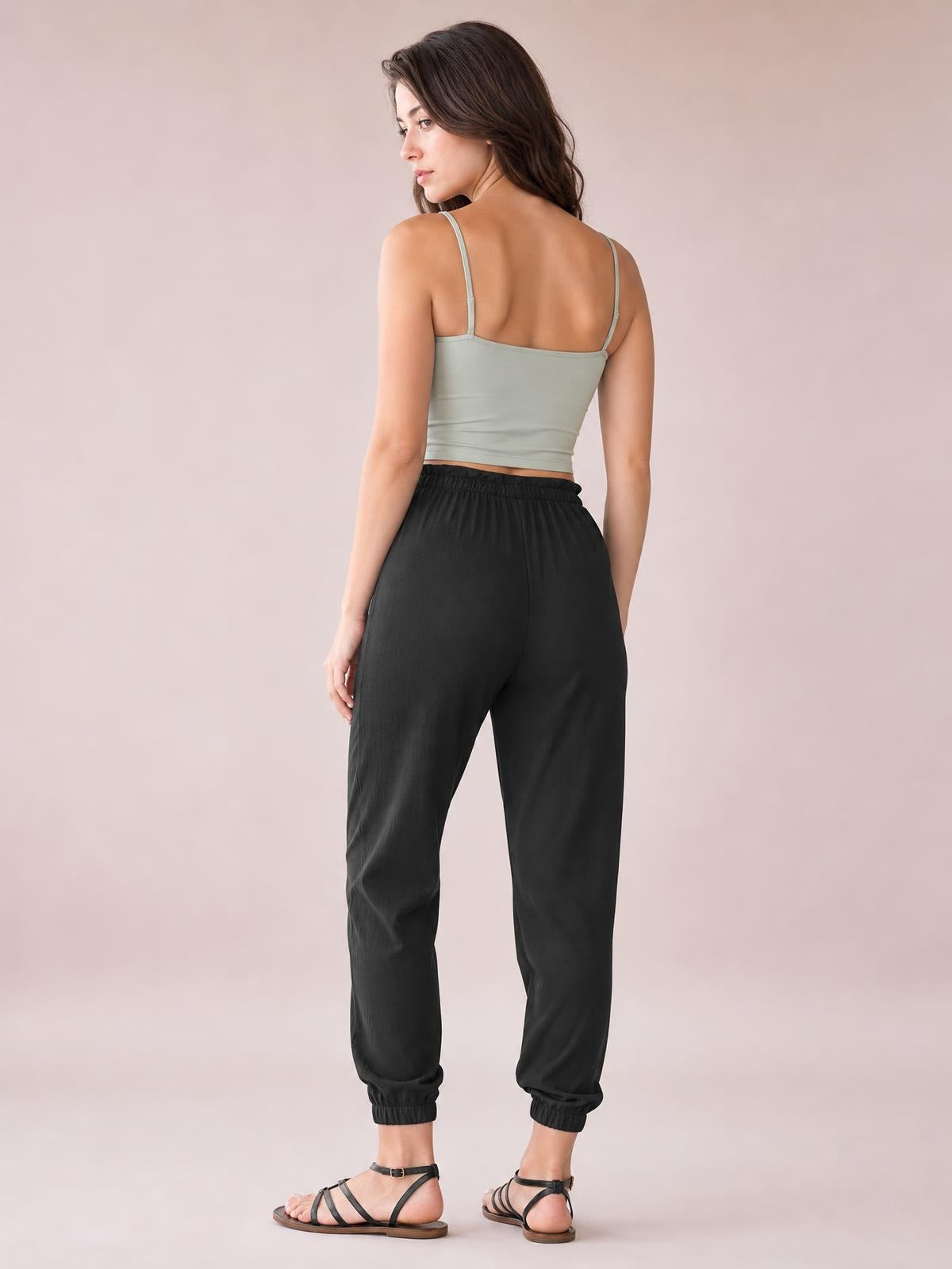 Model shown from behind wears solid black high waist joggers with an elastic waistband, side pockets, relaxed tapered legs, and ribbed ankle cuffs.
