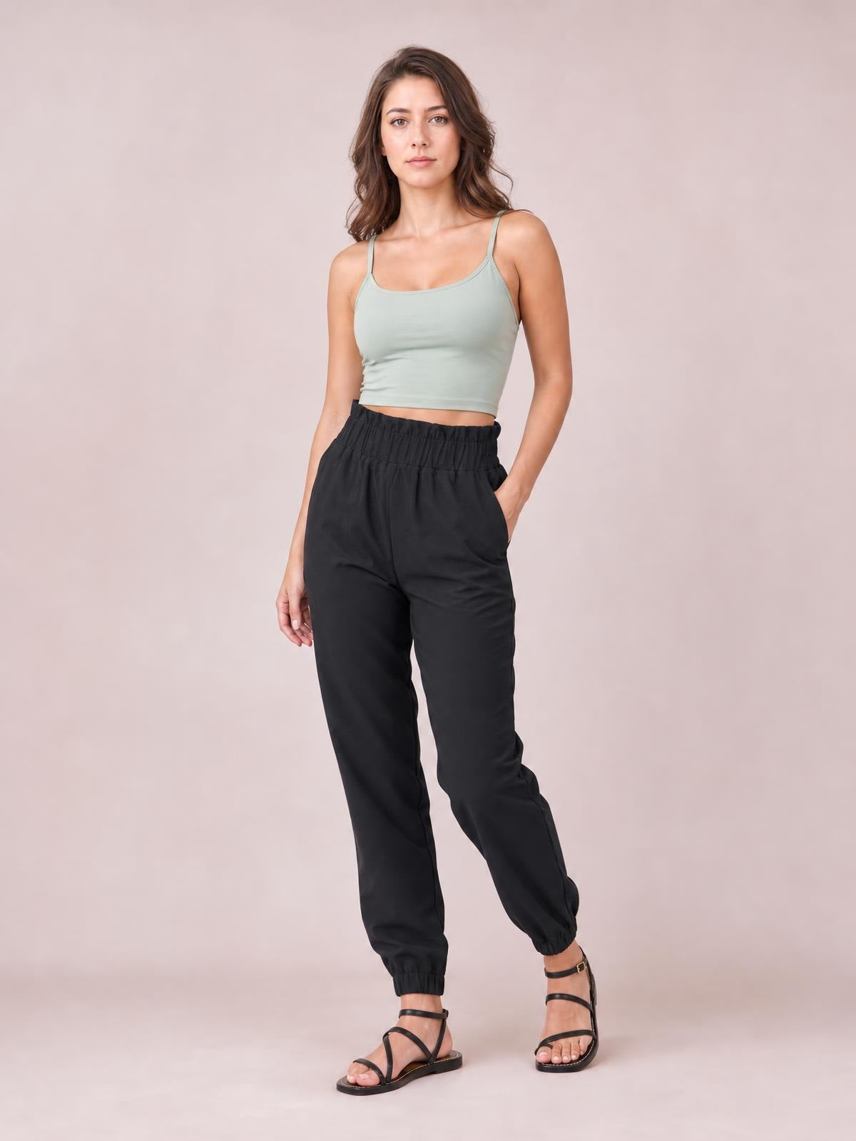 Model standing in black high waist joggers with side pockets, a relaxed long-leg silhouette, gathered waistband, and elasticized cuffs.