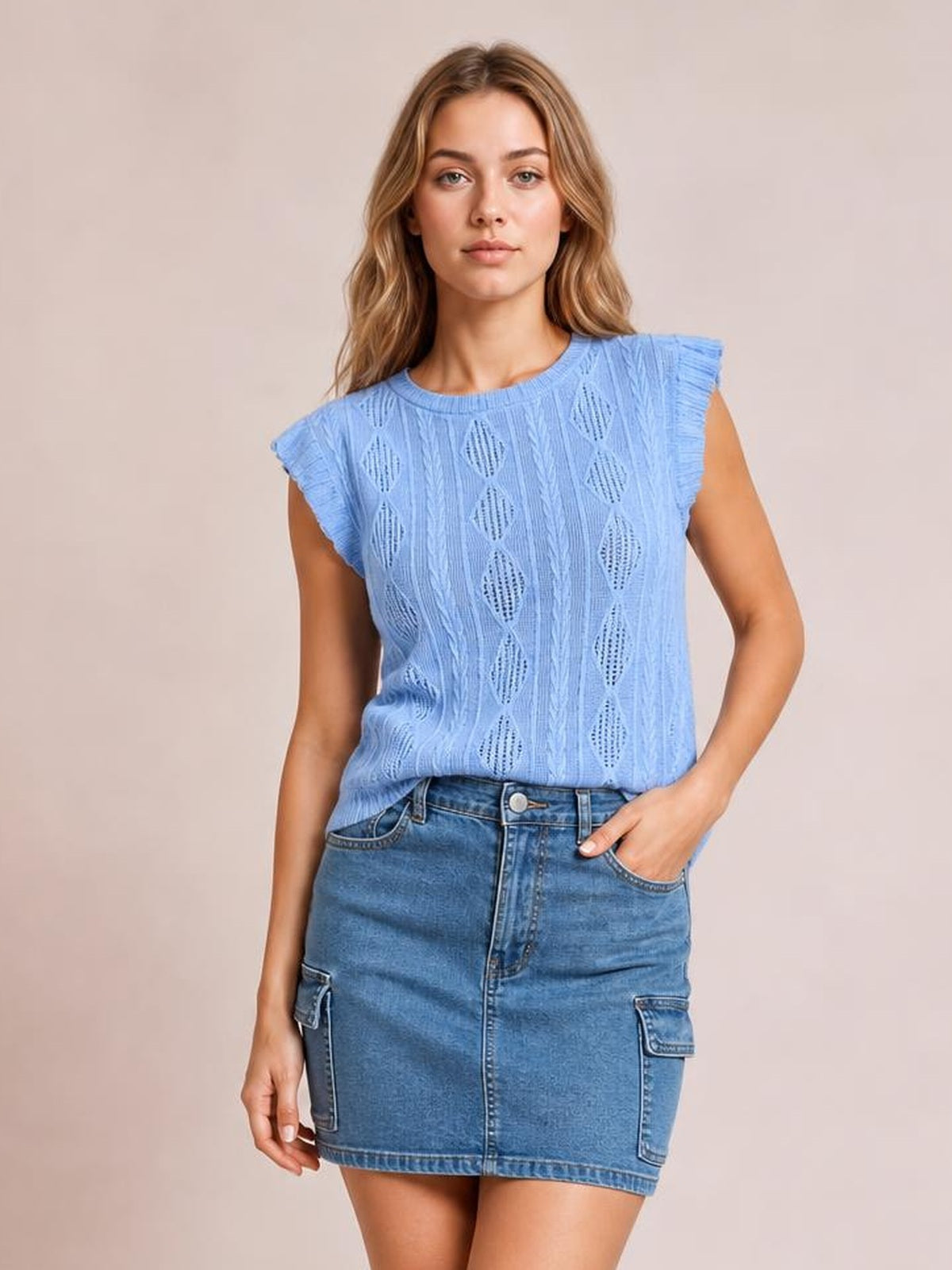 A model stands with one hand in a pocket, wearing a high-waist blue denim skirt with a straight mini silhouette, front closure, and cargo-style patch pockets.