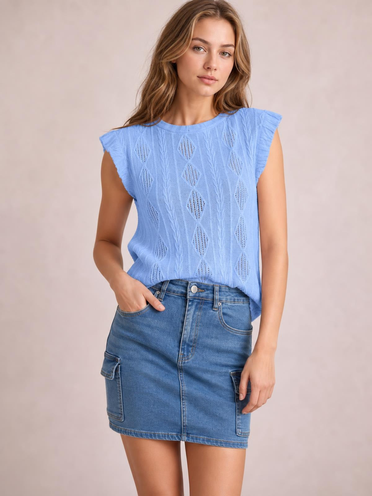 A model wears a blue high-waisted denim mini skirt with a straight silhouette, button-fly front, stitched seams, and large patch pockets, one hand tucked inside.
