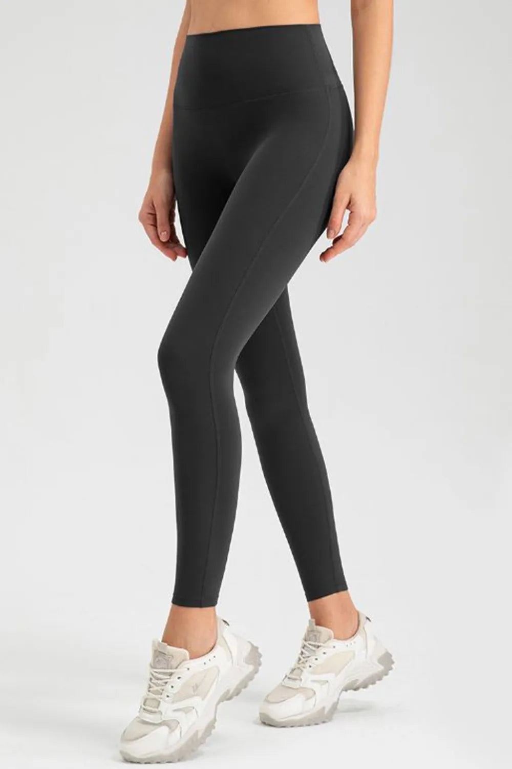 Model wearing black high-waist skinny active pants with a smooth fitted silhouette and subtle curved seam detail, standing with one leg crossed.