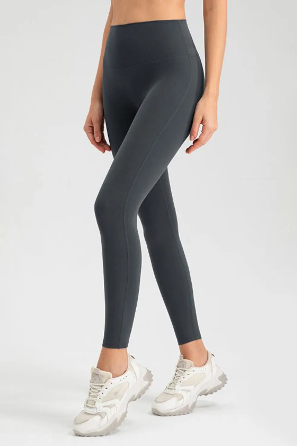Model crossing her legs wears dark high-waist skinny active pants with a sleek, stretchy silhouette, fitted seams, and ankle-length hems.