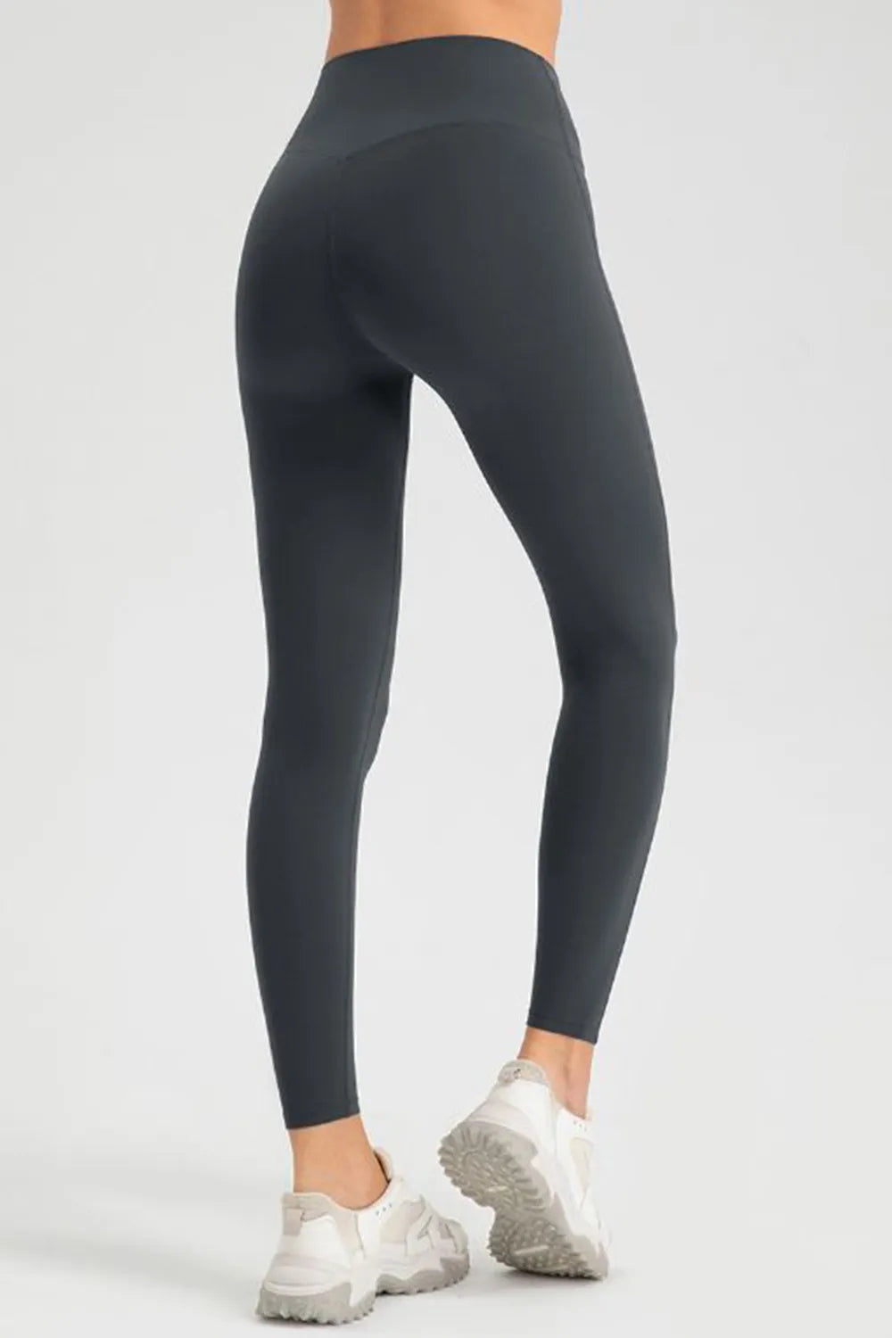 Model in a turned pose wears black high-waist skinny active pants with a sleek, stretchy full-length legging silhouette and fitted construction.