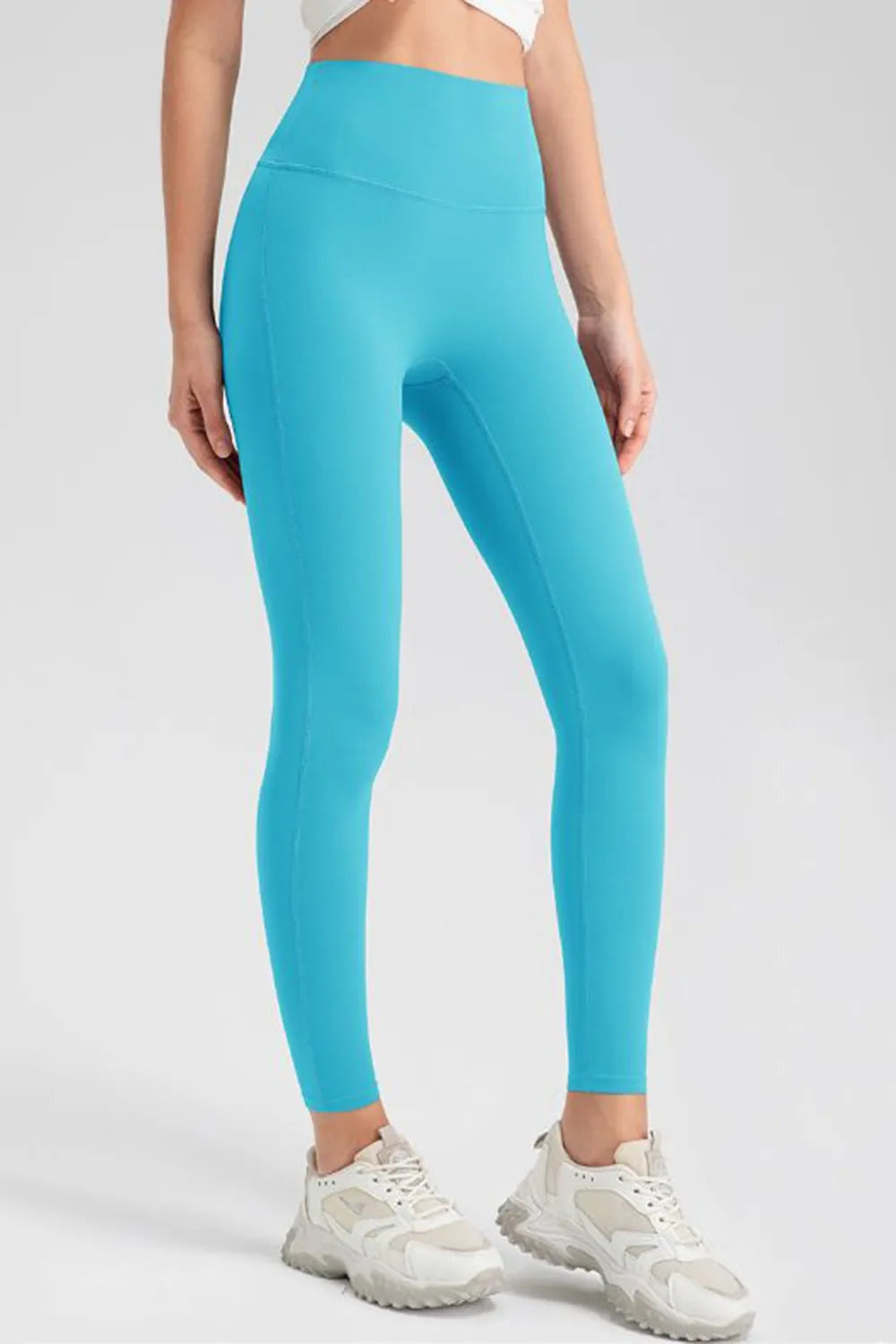 Model stands with hands at her hips wearing bright turquoise high-waist skinny active pants with a smooth, stretchy, ankle-length legging silhouette.