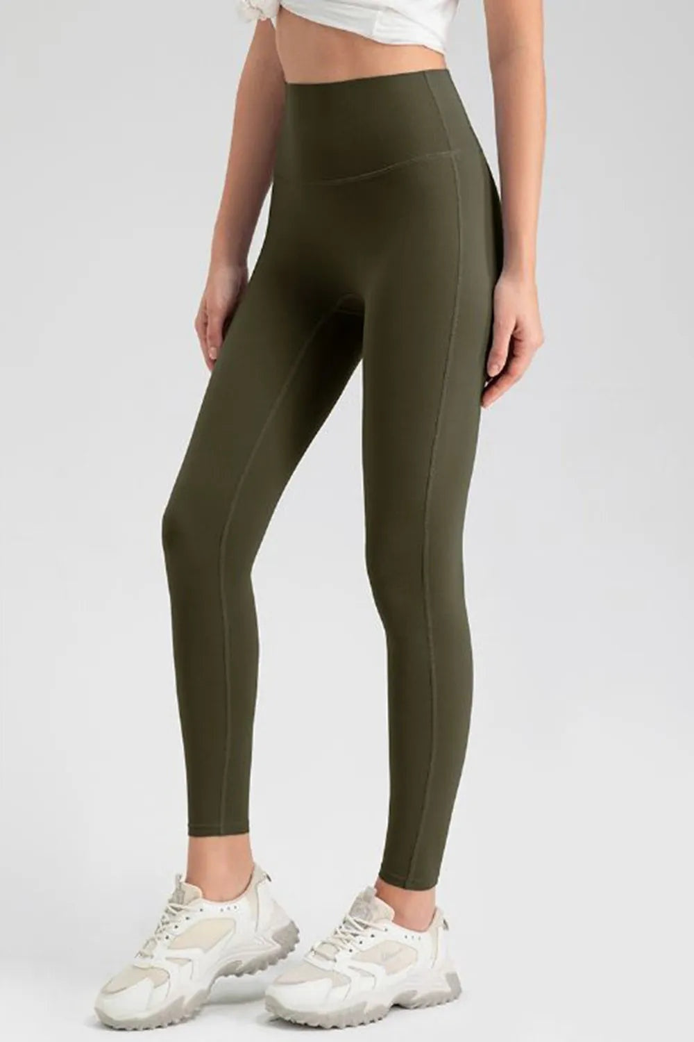 Model stands with one leg angled in olive green high-waist skinny active leggings featuring a smooth stretch fit, ankle-length silhouette, and subtle seam detailing.