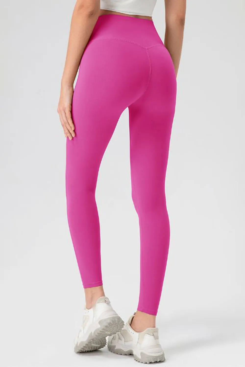 Model poses from the back in bright pink high-waist skinny active leggings with a close-fitting stretch silhouette and curved rear seam.