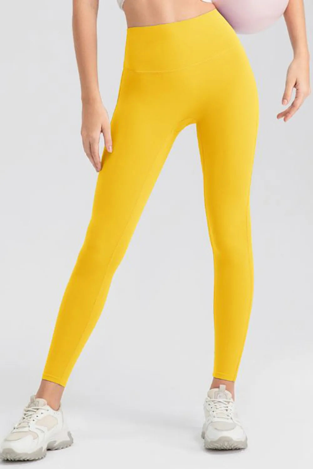 Model wearing bright yellow high-waist skinny active pants with a smooth wide waistband, stretch fit, and full-length tapered silhouette, standing with legs apart.
