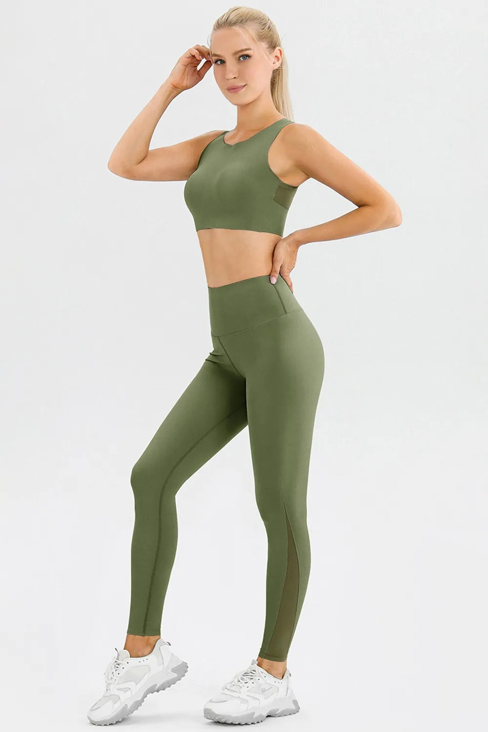A model poses in olive green high-waist skinny active pants with a wide waistband, fitted full-length silhouette, and one leg bent.