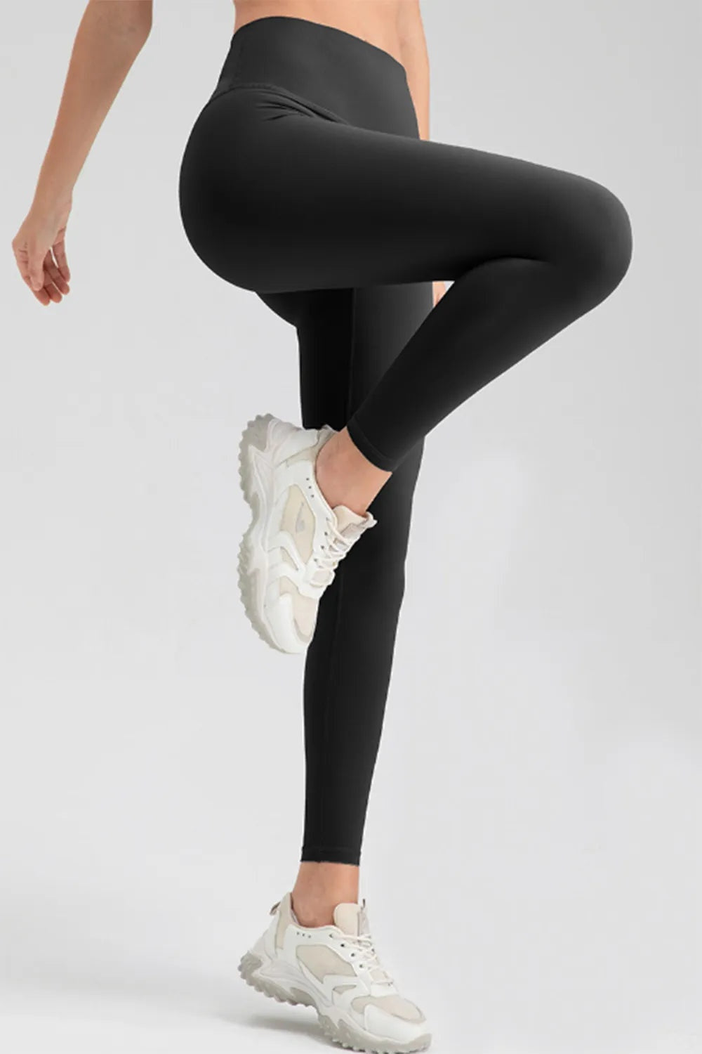 A model poses in black high-waist skinny active pants, featuring a smooth, highly stretchy, close-fitting legging silhouette while balancing with one knee raised.