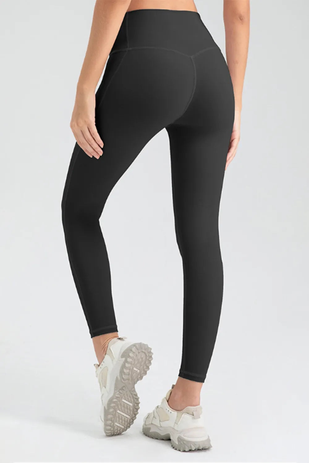 A model poses in black high-waist skinny active pants with a sleek ankle-length silhouette, stretch fit, curved seat seam detailing, and one leg lifted.