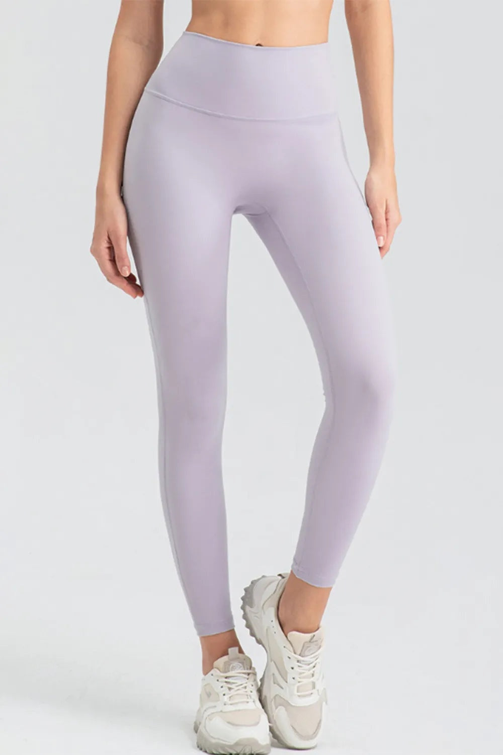 Model wearing lilac high-waist skinny active leggings with a smooth, fitted ankle-length silhouette and wide contoured waistband, standing with one leg crossed.