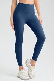 Model wears navy blue high-waist skinny active pants with a smooth fitted silhouette, ankle-length legs, and a wide seamed waistband while standing with one knee bent.