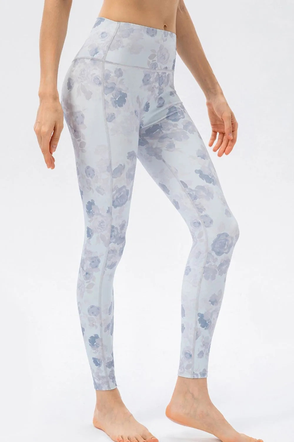 Model poses in high-waist skinny active leggings with a pale blue and gray floral print, fitted silhouette, stretch fabric, and visible seam construction.