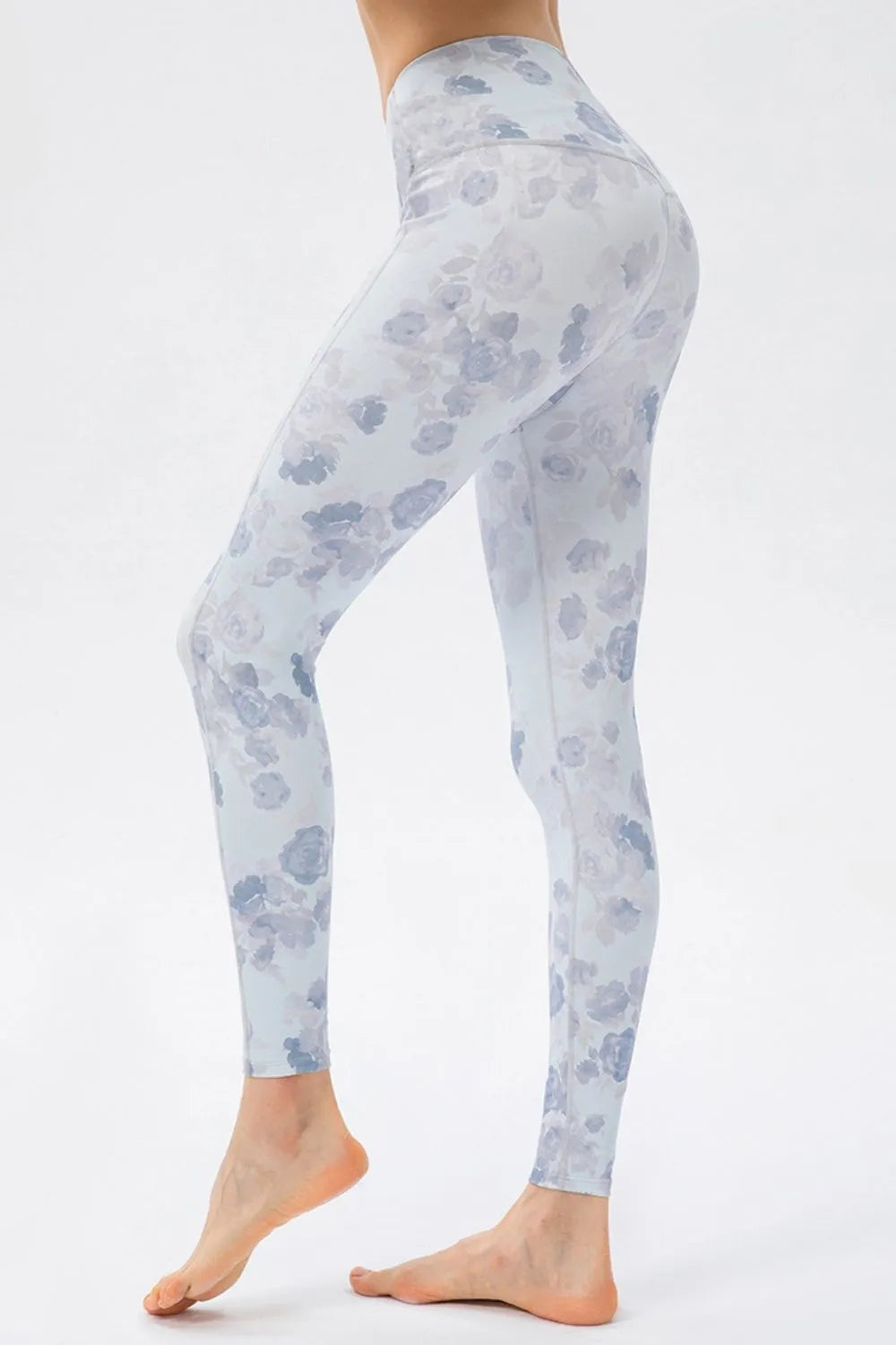 A model wears pale blue floral high-waist skinny active pants with a fitted ankle-length silhouette, standing with one foot raised to show the stretch leggings.