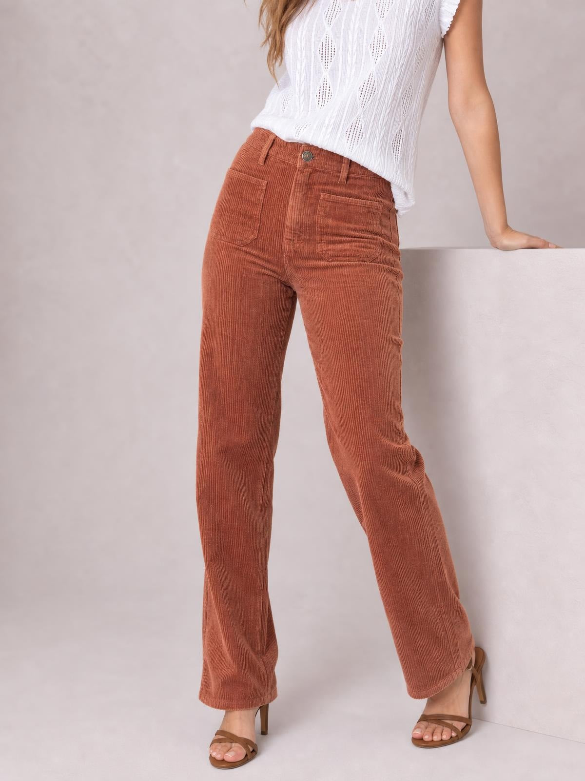 A model wears high-waist rust-brown corduroy pants with square front pockets, belt loops, a button closure, and a straight-leg silhouette.