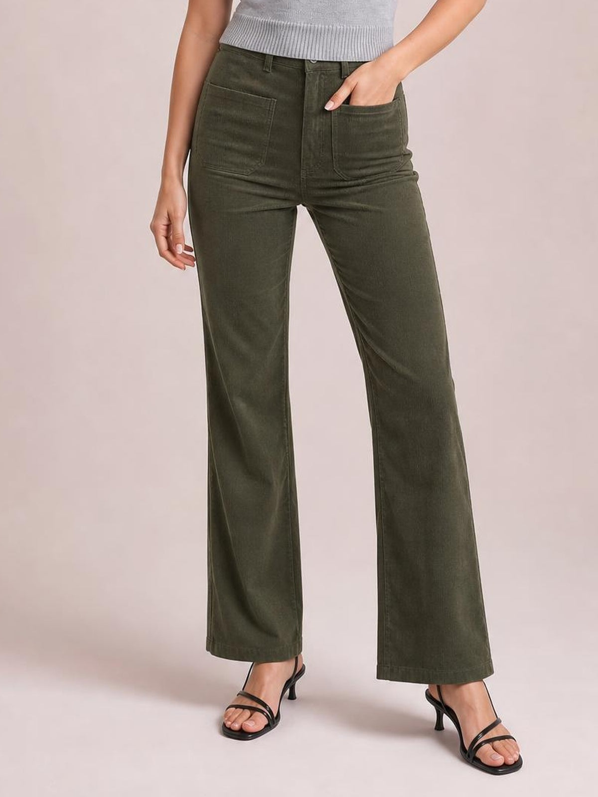 Model wears olive green high-waist corduroy pants with square front pockets, a button fly, and a relaxed straight-leg silhouette, one hand tucked inside.