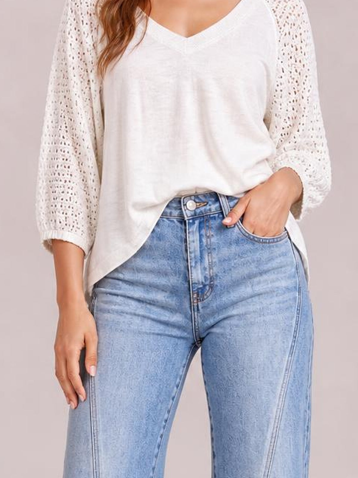Model tucks one hand into the pocket of light-wash high-waist straight-leg jeans, showing the button closure, belt loops, front pockets, and structured silhouette.
