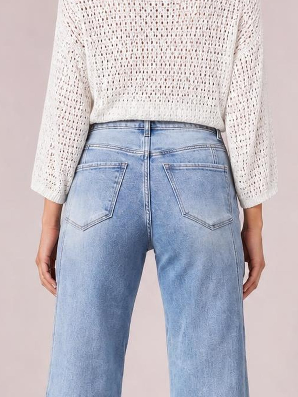 A rear view shows a model wearing light blue washed high-waist straight jeans with belt loops, contrast stitching, and two angular back pockets.