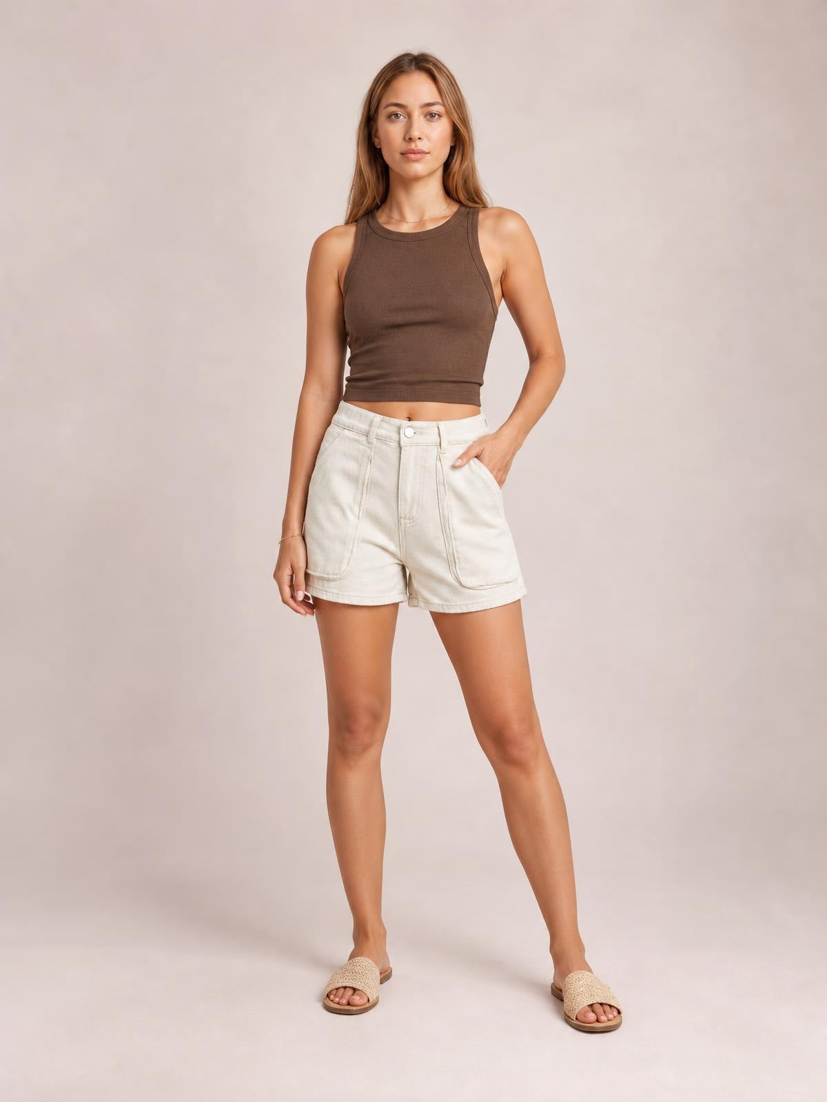 A model stands with one hand in the pocket, wearing high-waist cream denim utility shorts with a V-front, oversized patch pockets, and a relaxed silhouette.