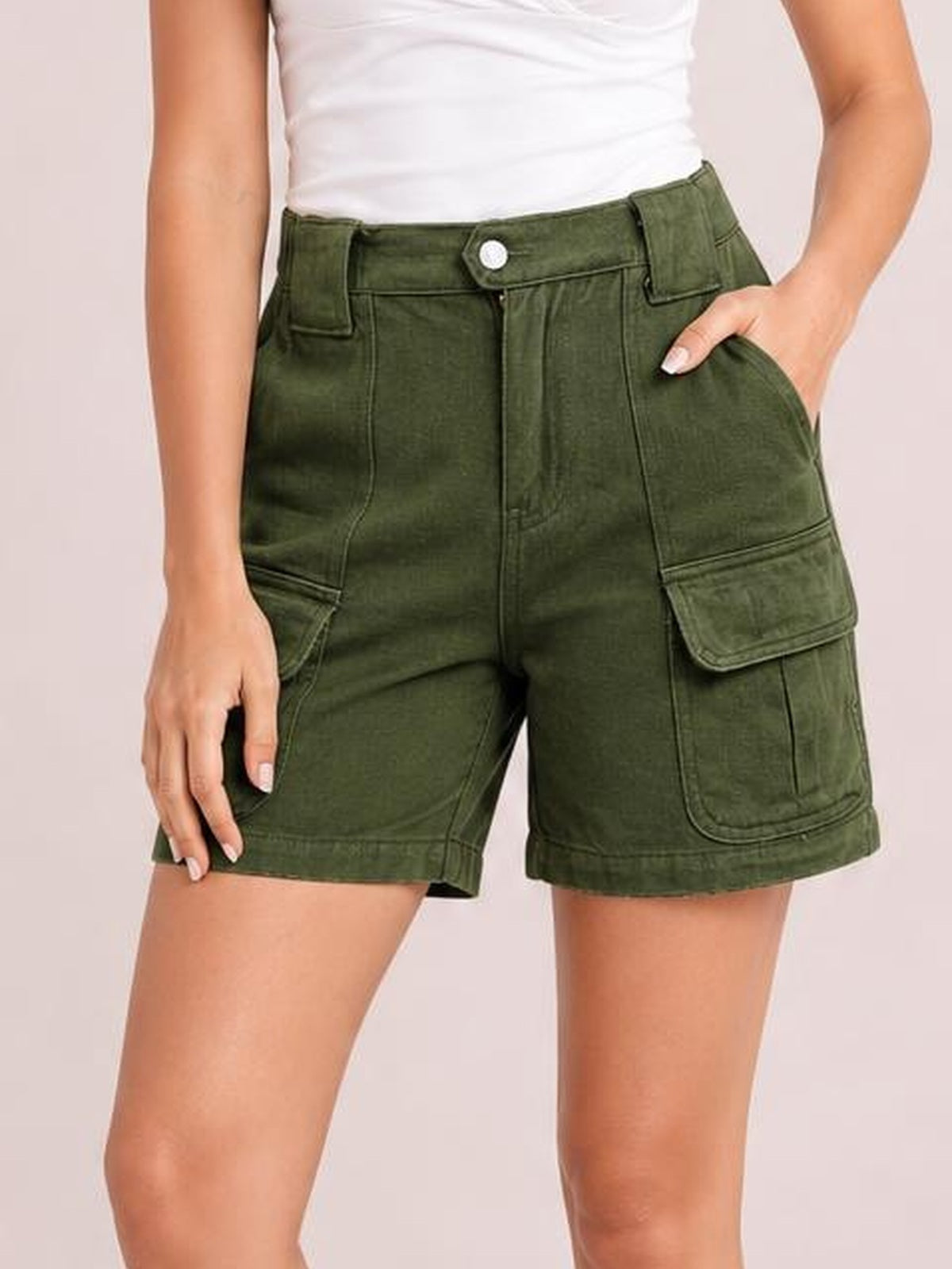 A model wears olive green high-waist washed denim shorts with a structured mid-thigh silhouette, button closure, belt loops, front pockets, and flap cargo pockets.