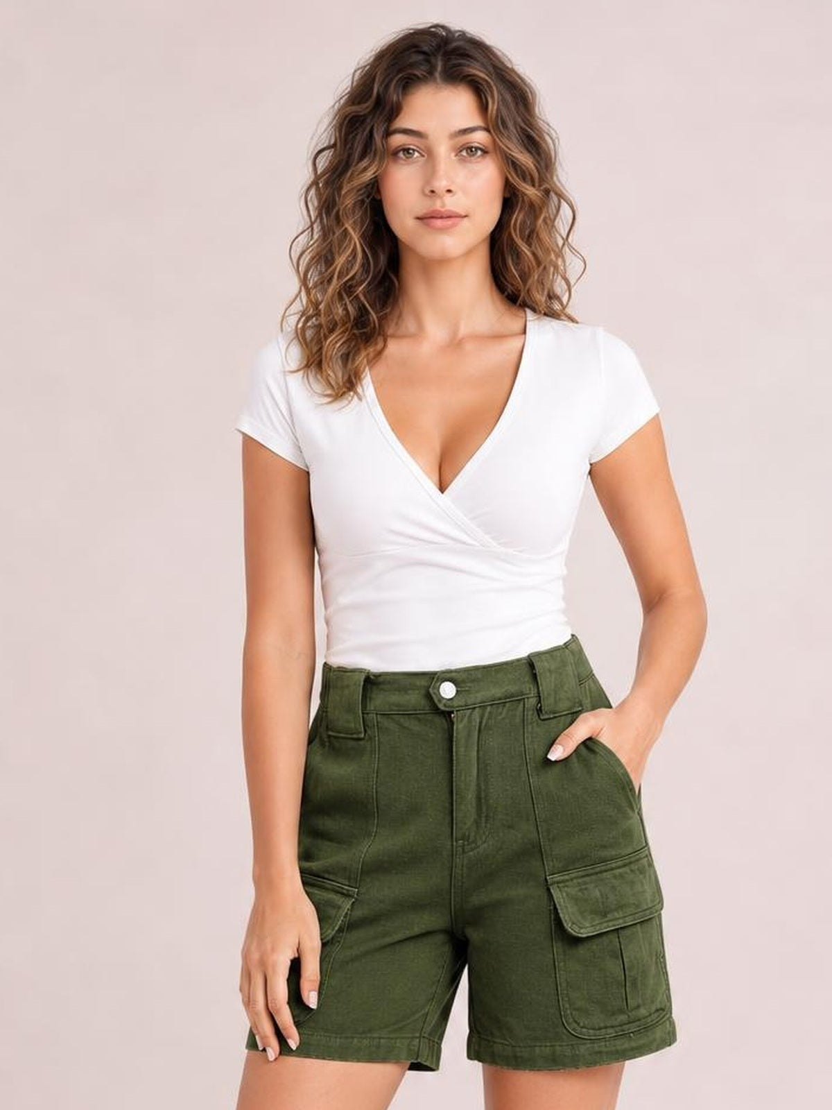 A woman modeling a white wrap-style short-sleeve top and olive green cargo shorts against a solid pale pink background.