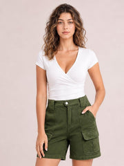 A woman modeling a white wrap-style short-sleeve top and olive green cargo shorts against a solid pale pink background.