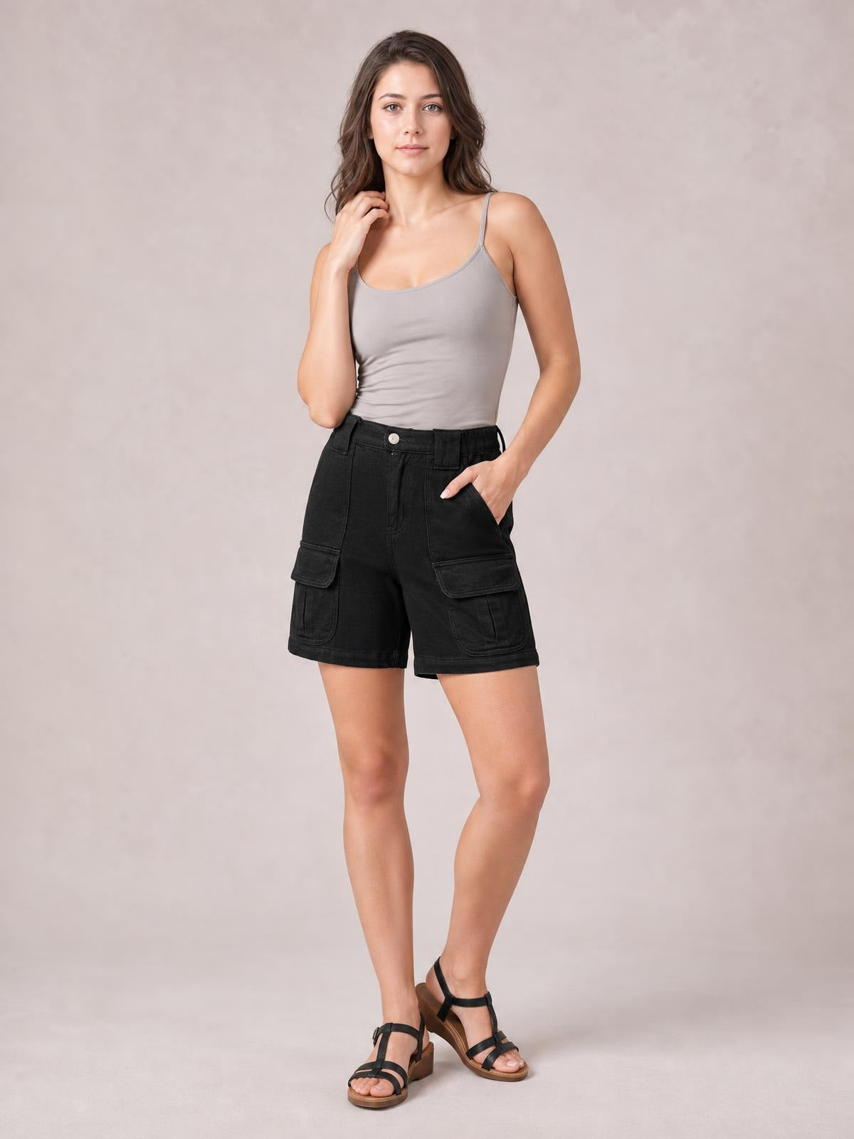 A model poses with one hand in the pocket, wearing black high-waist washed denim shorts with belt loops, cargo-style flap pockets, and a straight hem.
