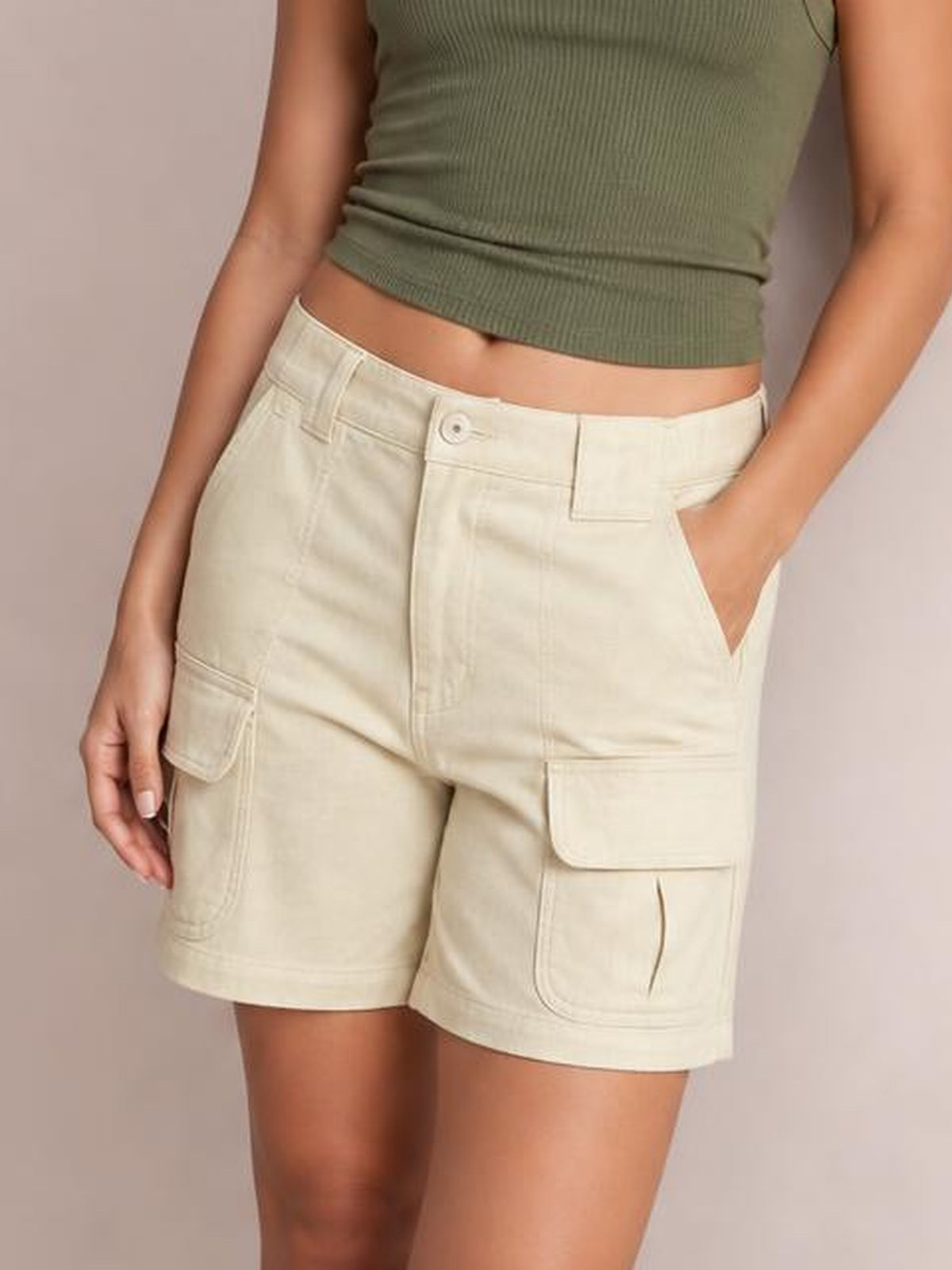 A model wears light cream high-waist washed denim shorts with belt loops, button fly, angled pockets, cargo patch pockets, and a relaxed silhouette.