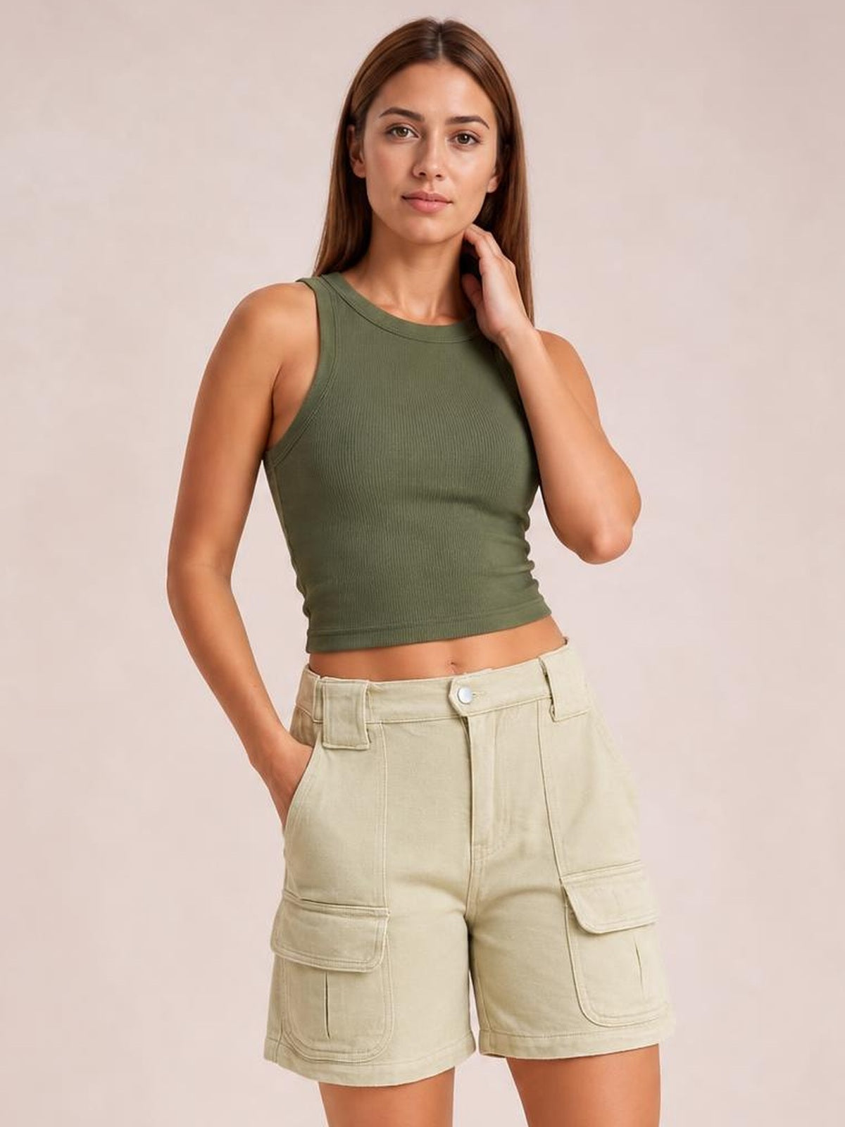 A woman modeling a sleeveless olive green ribbed crop top and light beige cargo shorts against a solid light beige studio background.