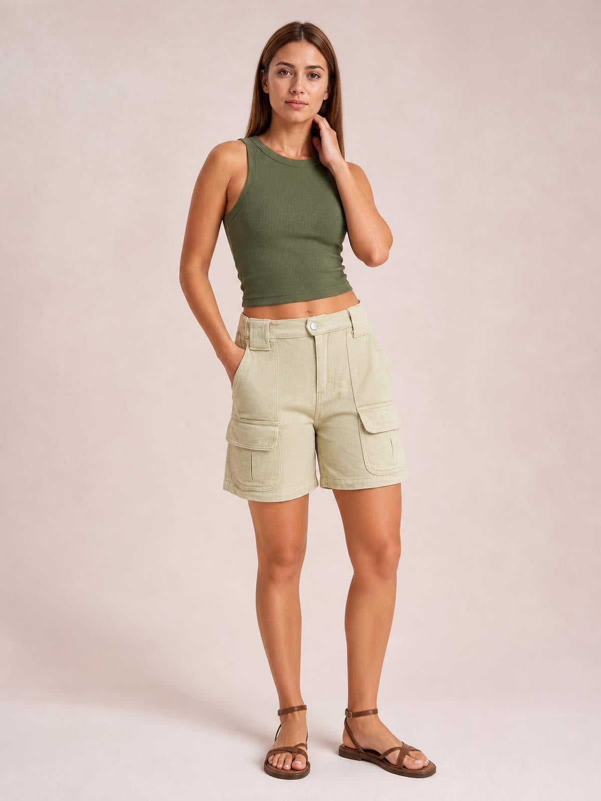 A model poses in high-waist washed denim shorts with a relaxed silhouette, button closure, belt loops, side pockets, and large flap cargo pockets.