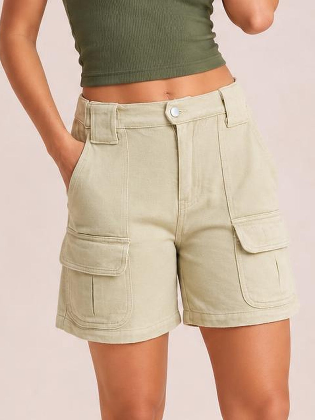 A model wears high-waist washed denim shorts in pale beige with a relaxed straight-leg silhouette, button closure, side pockets, and large cargo patch pockets.