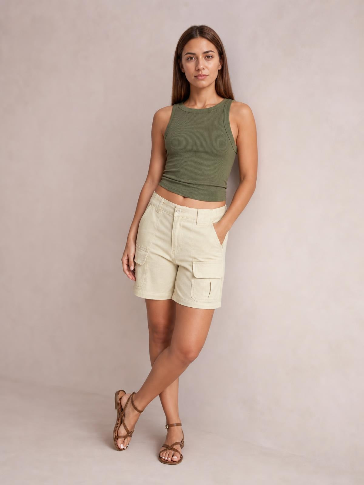 A model poses with crossed legs and one hand in the pocket, wearing light cream high-waist washed denim shorts with a straight fit and cargo pockets.