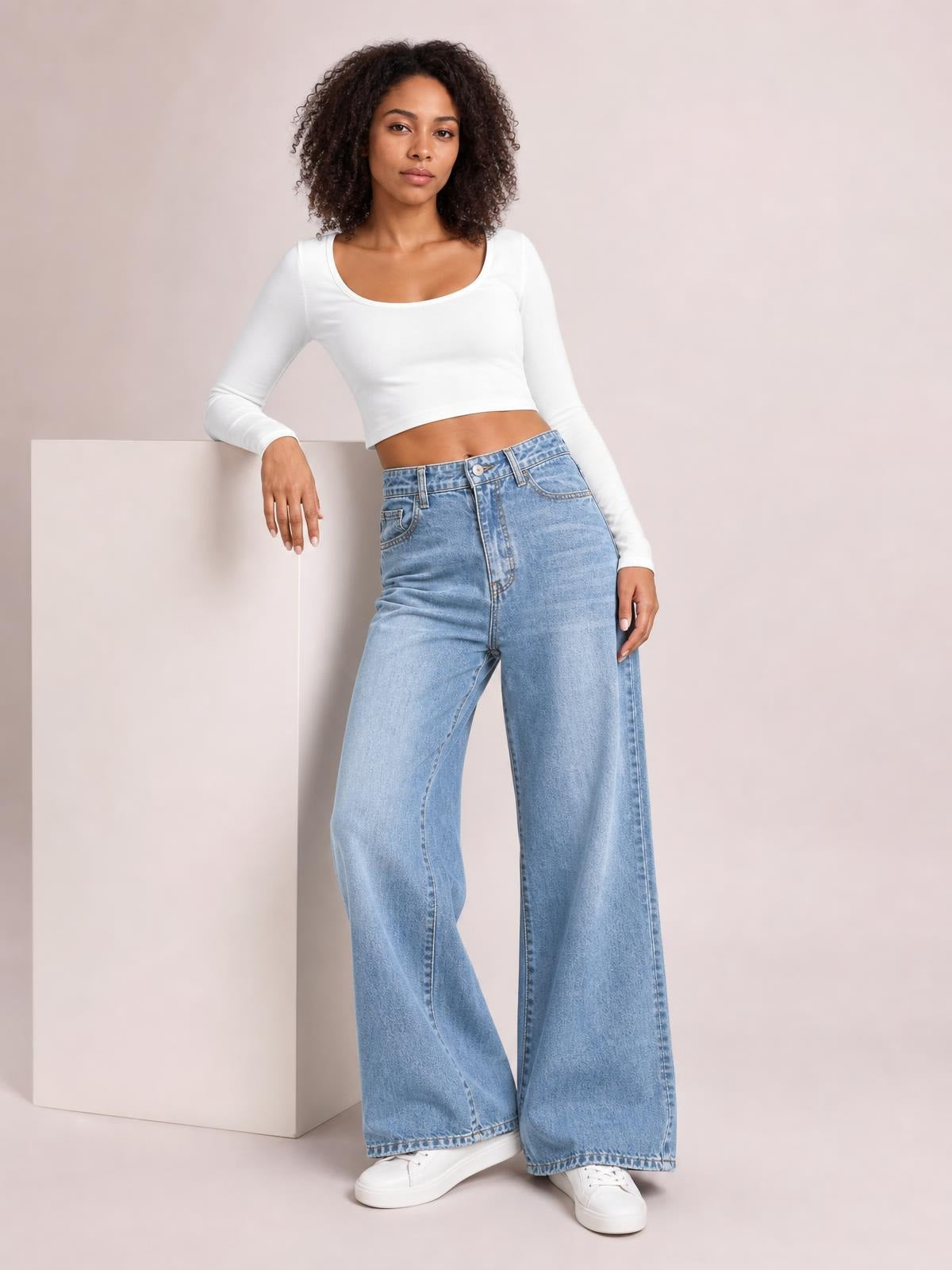 Model poses beside a pedestal wearing light blue high waist wide leg jeans with belt loops, front pockets, button closure, zip fly, and full-length hems.