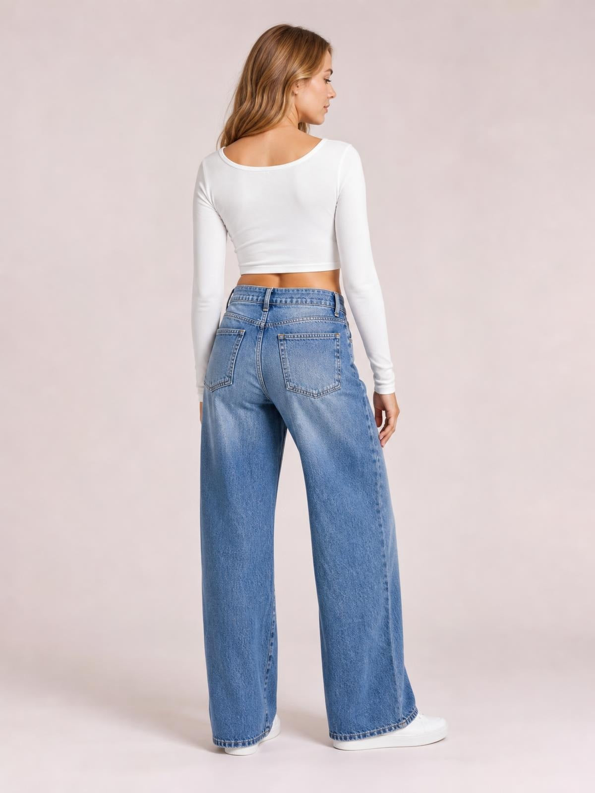 Model turned slightly away showcases light blue high-waist wide-leg jeans with belt loops, button closure, back pockets, and a relaxed floor-length silhouette.