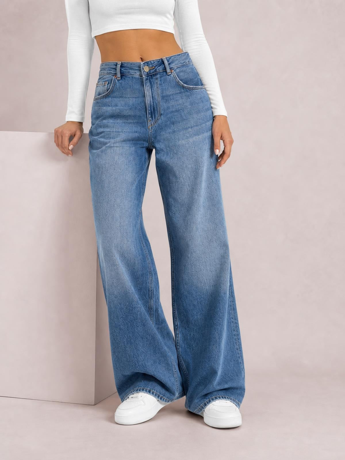 Model poses in light blue high waist wide leg jeans with a button fly, belt loops, front pockets, and relaxed full-length silhouette.