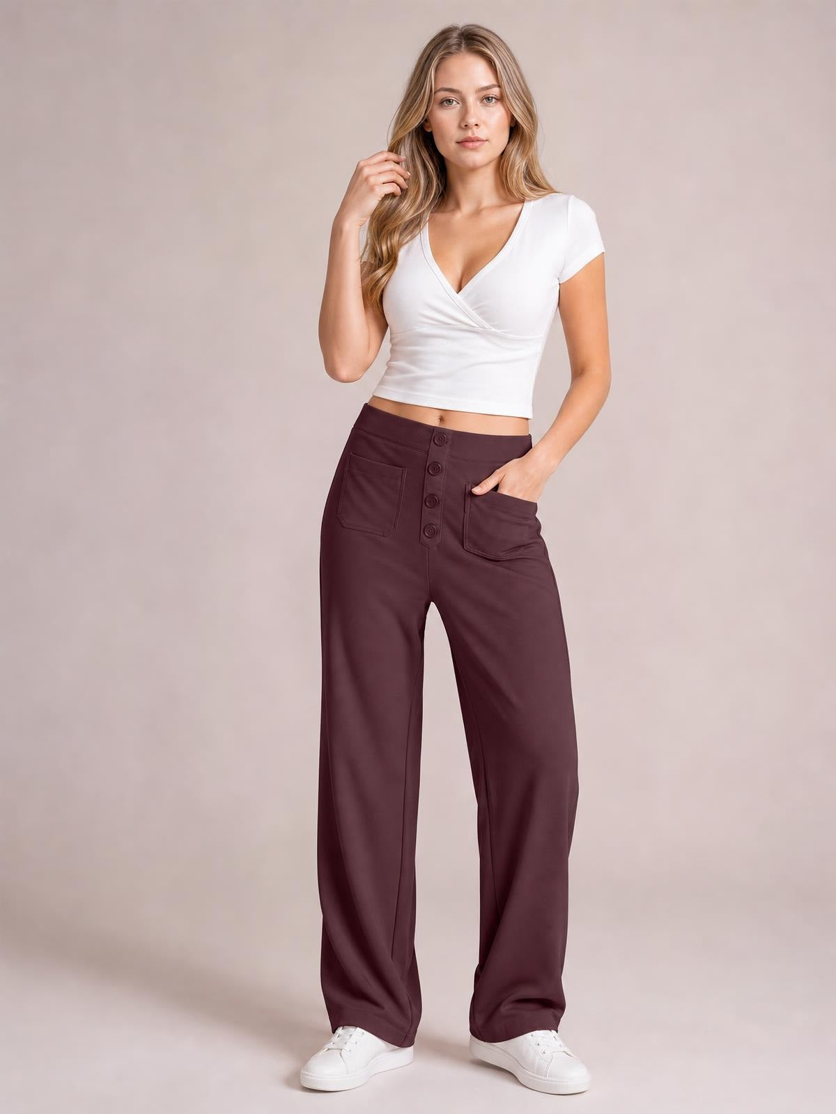 Model poses with one hand in the pocket of burgundy high-waist wide-leg pants featuring front patch pockets, button closure, and a relaxed full-length silhouette.