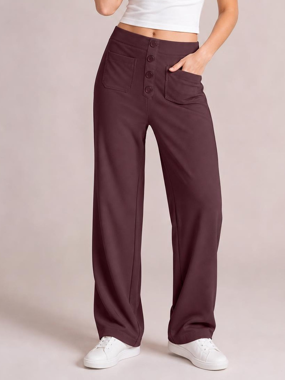 A model stands in plum high waist wide leg pants with front patch pockets, a button fly, and a relaxed silhouette, one hand tucked into a pocket.