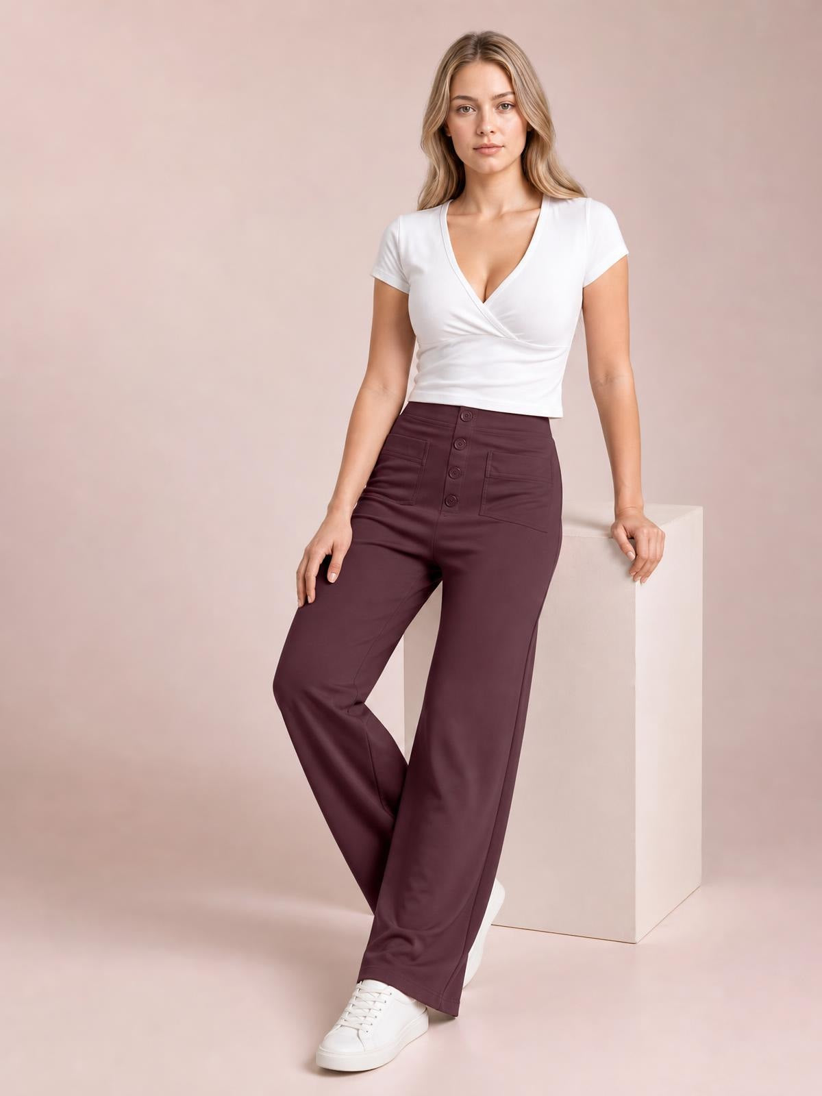 A model poses in burgundy high waist wide leg pants with front pockets, a button-front closure, and a smooth opaque silhouette.