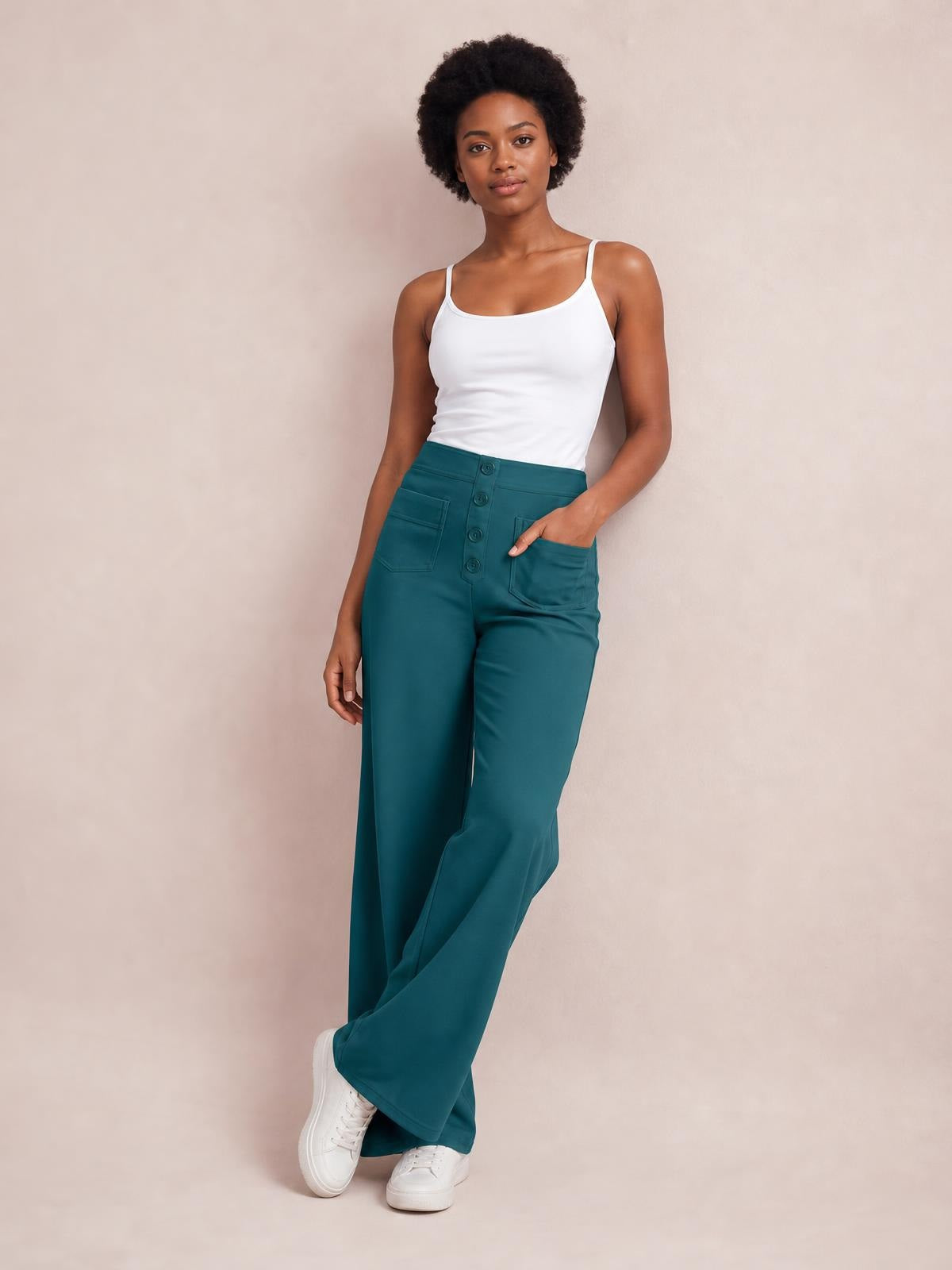 A model poses with one hand in the pocket of teal high waist wide leg pants, featuring a button-front closure and relaxed full-length silhouette.