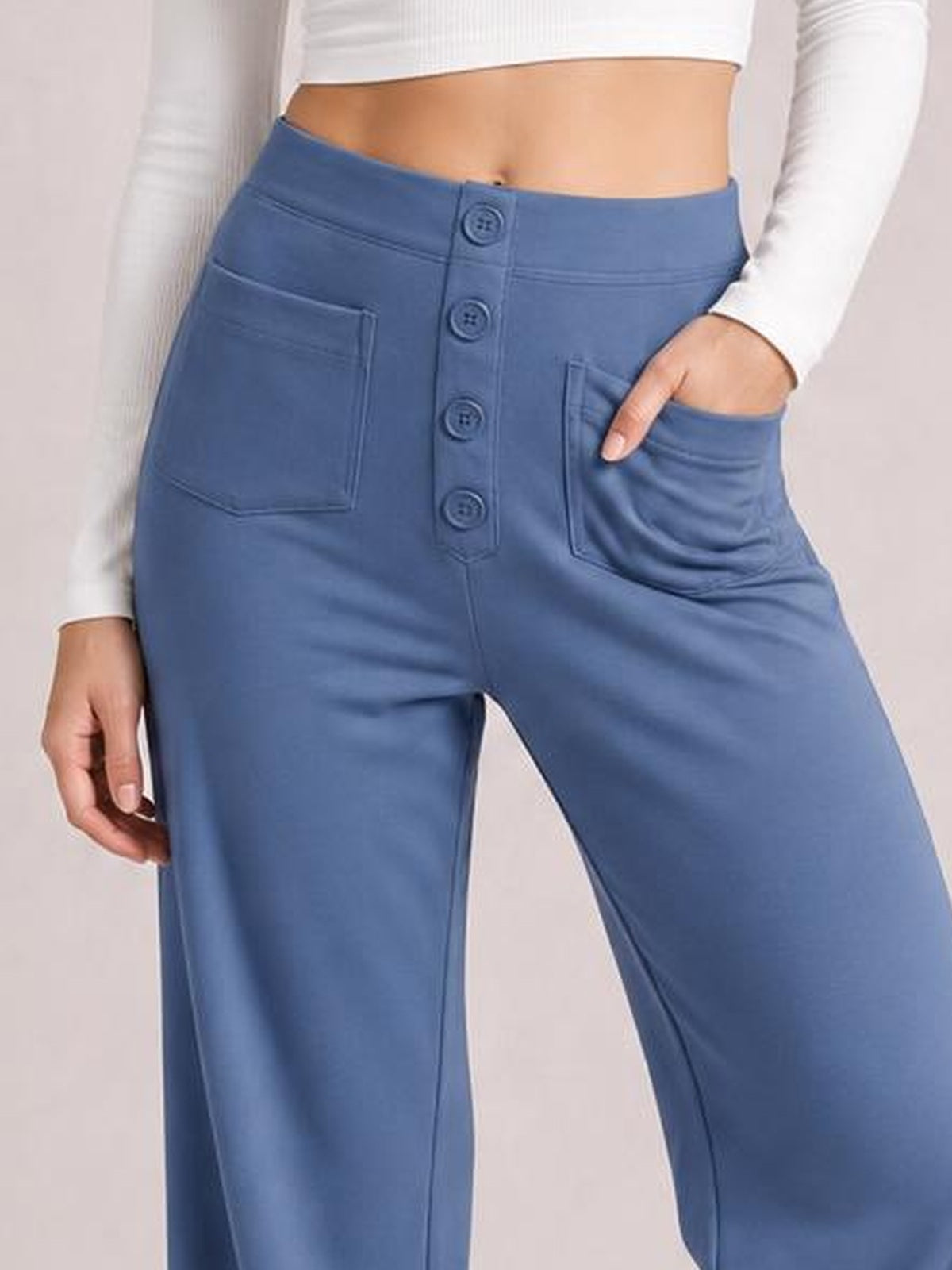 Model wearing blue high-waist wide-leg pants with front pockets, a button fly, and a relaxed silhouette, posing with one hand in a pocket.
