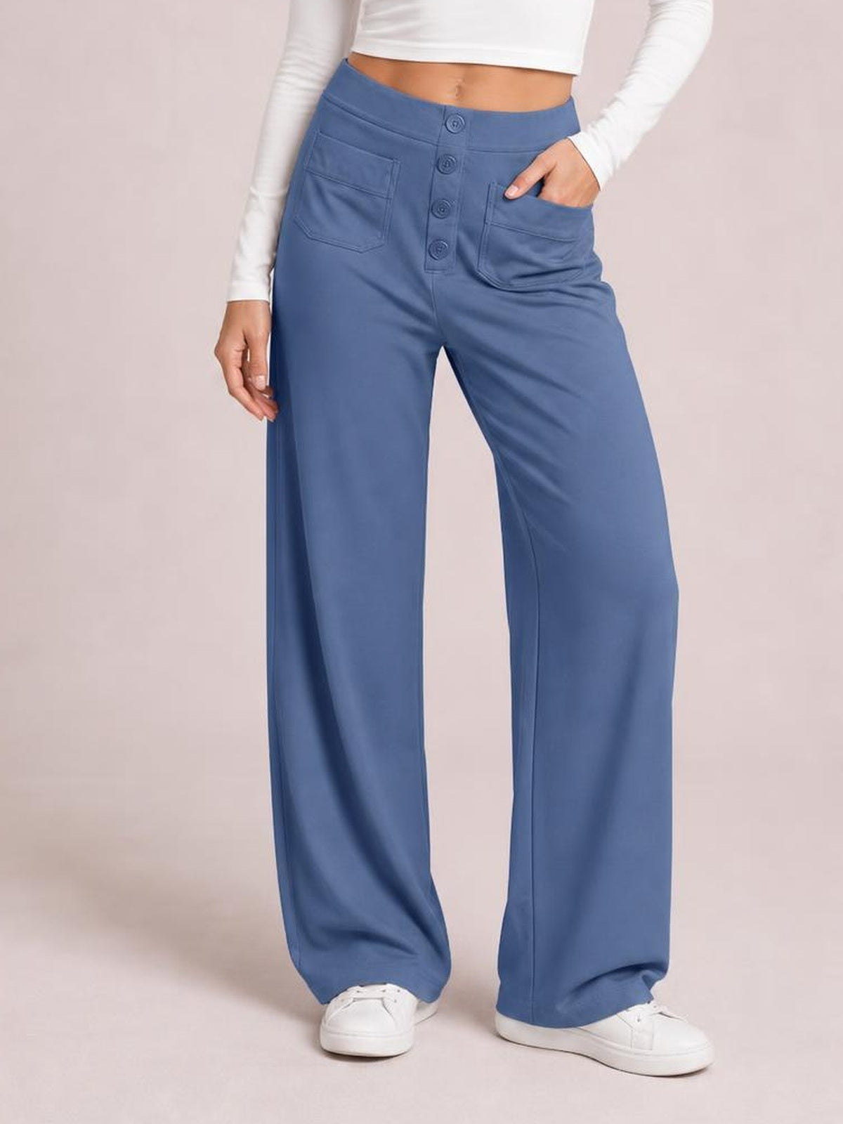 A model stands in blue high waist wide leg pants with a relaxed silhouette, front button closure, and convenient patch pockets, one hand tucked inside.
